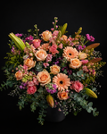 Bouquet with peach roses, pink stargazer lilies, peach gerbera daisies, pink roses, pink snapdragons, pink stocks, yellow golden rod, pink limonium and grey pennygum on a black background.