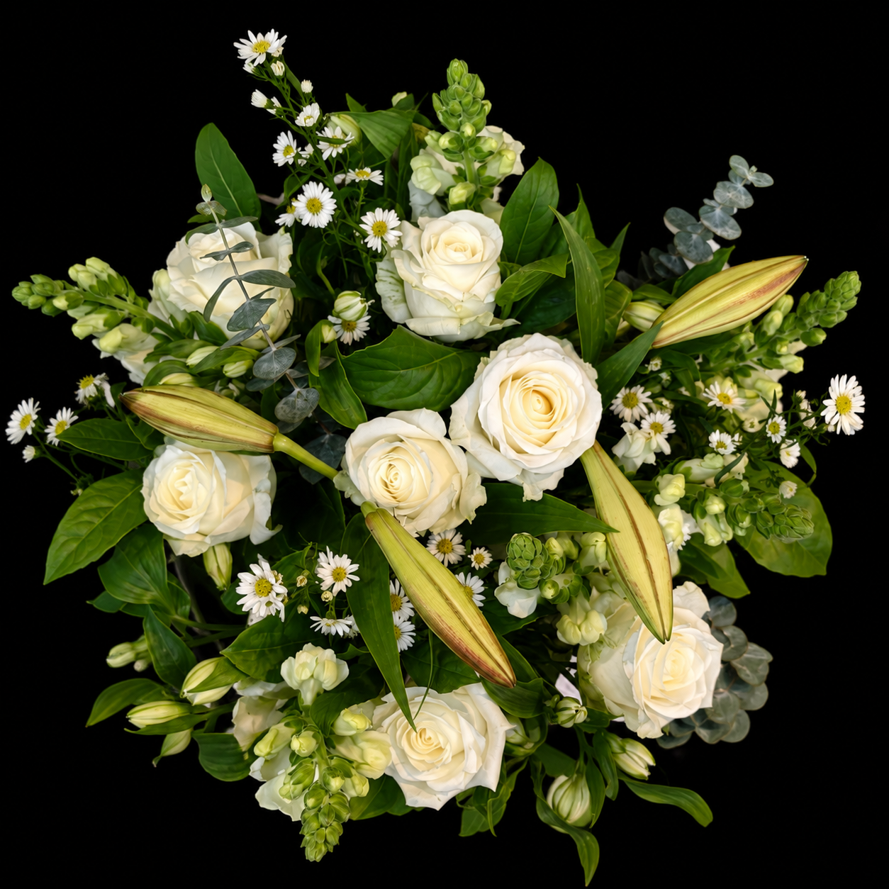 A dense floral bouquet featuring white roses, white lilies, small white daisies, and green foliage, photographed from above against a solid black background by Blooms Gifts Etcetera.